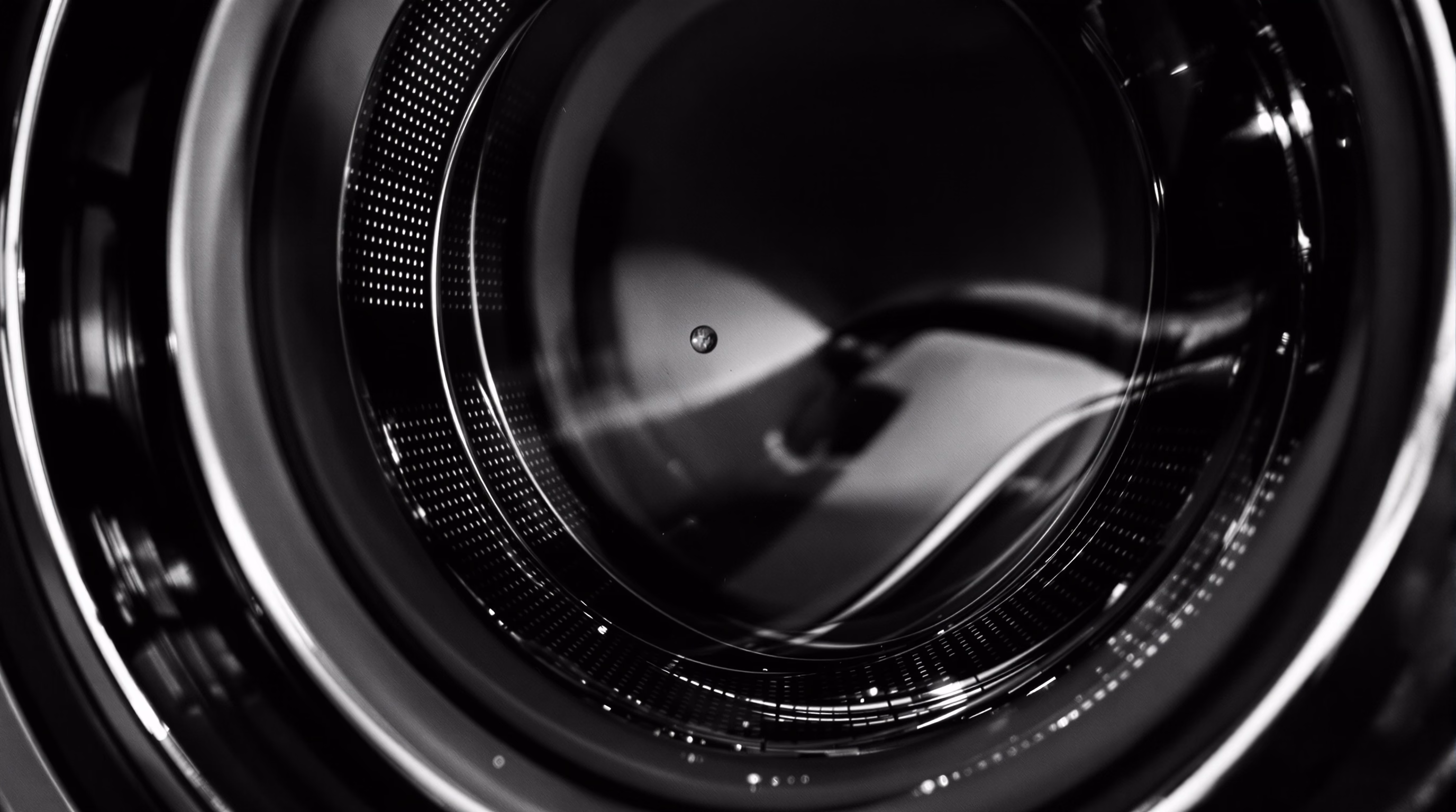 The steel drum interior of a large domestic washing machine in macro detail, rings of perforations catching hard side-light.
